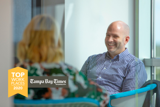 Man smiling while sitting across from a woman in conversation with Tampa Bay Times Top Workplaces 2020 logo overlayed