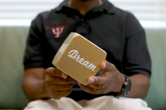 A person seated on a green sofa holding a cube with the word "Dream" printed on the visible side.