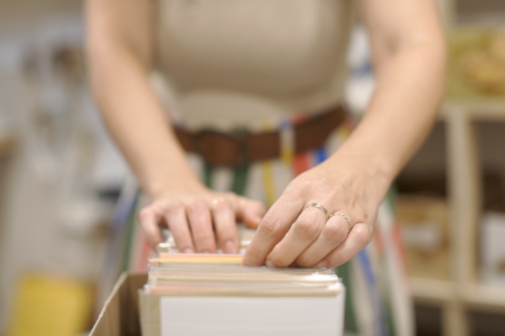 A person sorting through a box of bookmarks in a well-lit room with focus on hands.