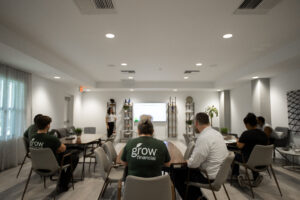 A presentation in progress at Grow Financial. A person is standing in front of a screen displaying a slide, addressing an audience seated at tables.