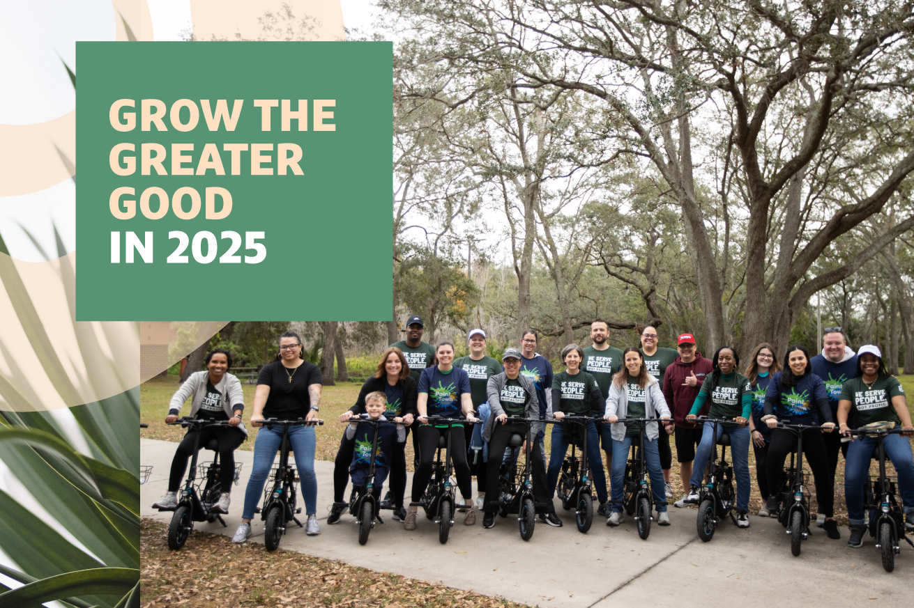 A group of people stands smiling behind a row of bicycles set against a backdrop of leafy trees, with text overlaid that reads "GROW THE GREATER GOOD IN 2025."